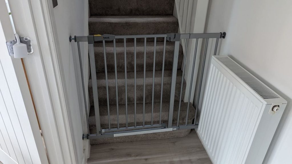 Grey metal safety baby gate locked at the bottom of a staircase, showing home proofing for 10 month old behaviour changes.