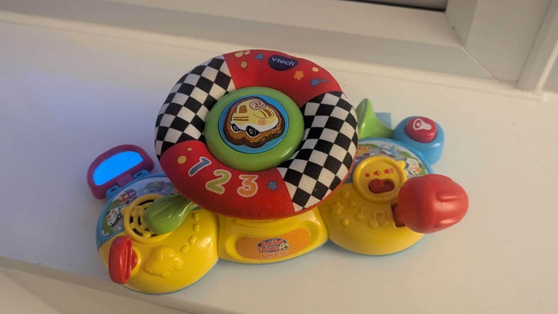 Colourful VTech Toot-Toot Drivers steering wheel toy sitting on a window sill for a stationary 9 month old baby.