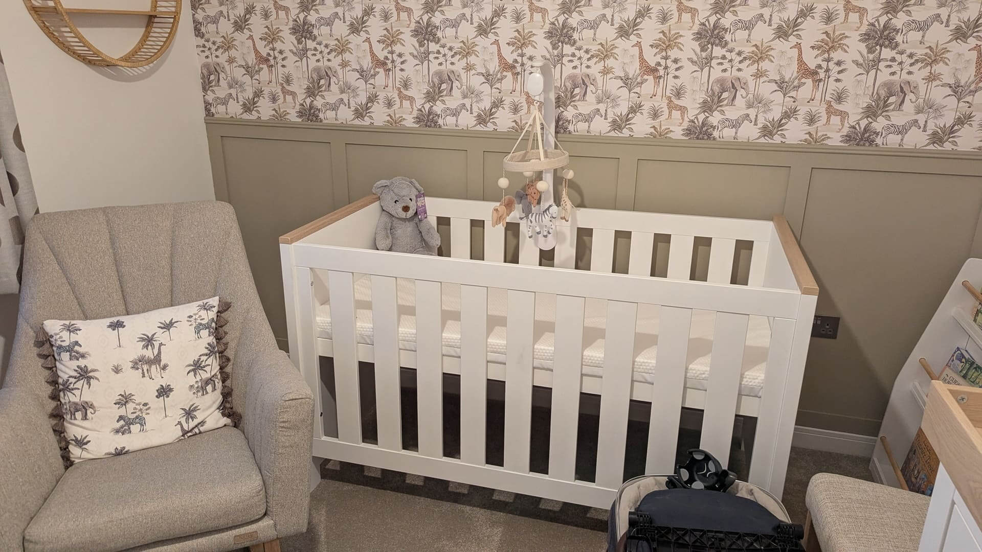 Completed white and oak baby cot in a decorated nursery with jungle wallpaper and a nursing chair—essential advice for expecting dads.