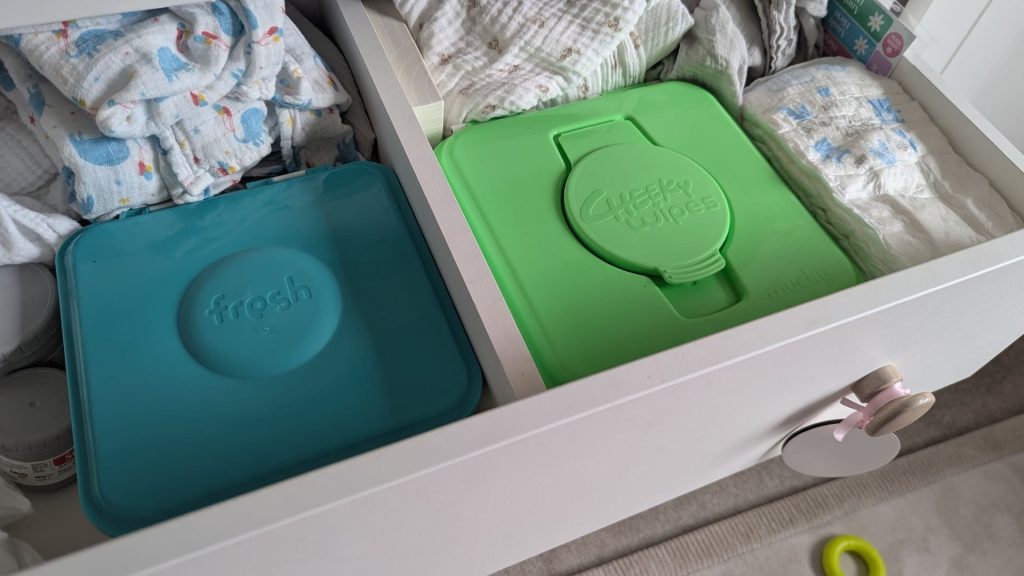 Close-up inside changing table drawer showing blue fresh wipes tub on left and green mucky wipes tub on right.