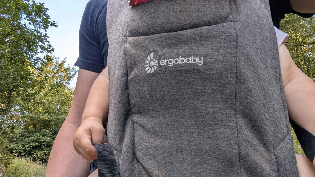 Close up of dad wearing Ergobaby Embrace carrier in Heather Grey showing logo and soft fabric