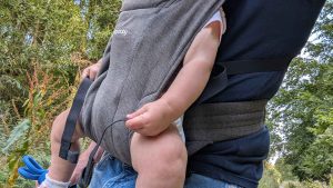 Side profile of baby carried in Ergobaby Embrace showing ergonomic M-position and waist support strap