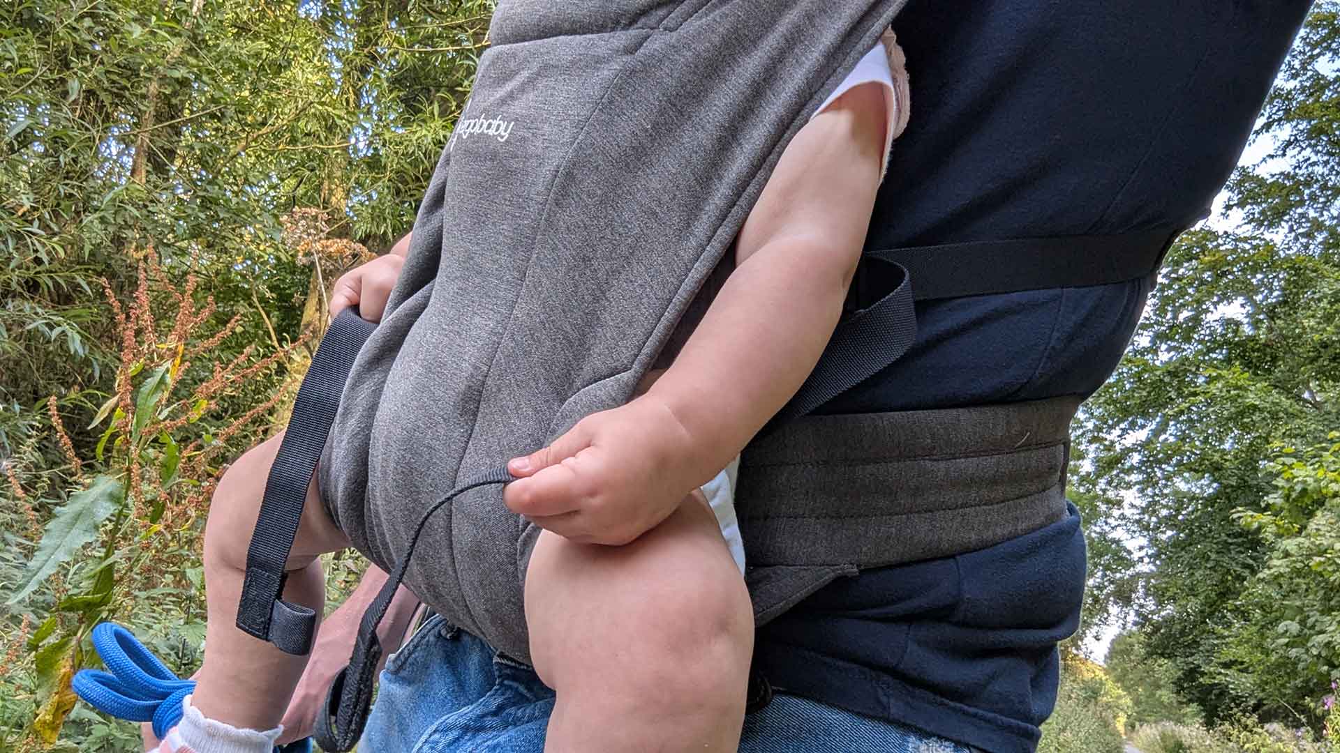 Side profile of baby carried in Ergobaby Embrace showing ergonomic M-position and waist support strap
