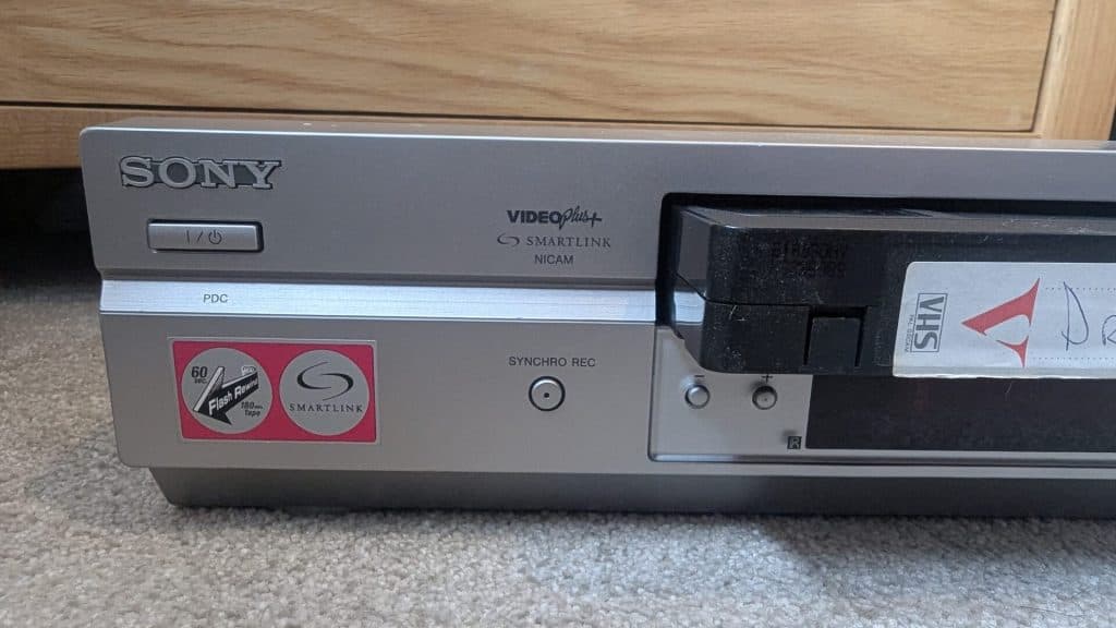 Front view of a silver Sony VHS VCR player with a tape partially inserted into the slot.