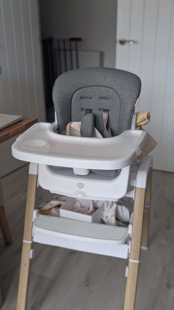 Front view of the grey Tutti Bambini Nova highchair sitting next to a dining table on a light wooden floor.