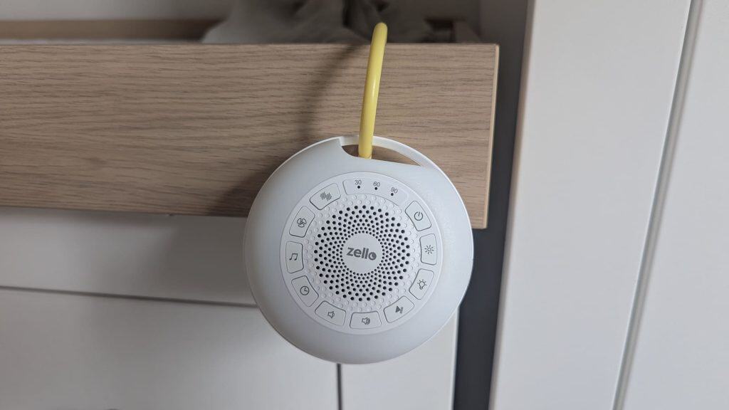 White Zello sound machine hanging from a wooden drawer unit using its yellow silicone strap.