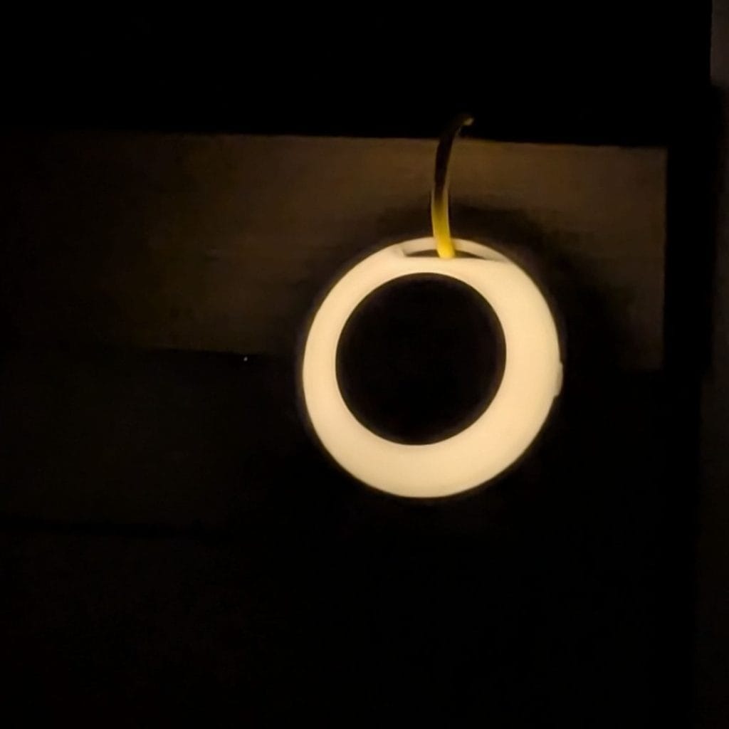 Circular Zello white noise machine glowing with a soft warm night light in a dark room.