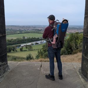 Dad standing at Penshaw Monument looking out at the Sunderland countryside view carrying an 11 month old baby in a Littlelife back carrier.
