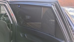 Custom-fit black Car Shades sun blind mounted inside the open rear door of a grey vehicle.