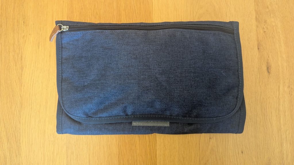 Dad's Emergency Car Kit for a Baby. Folded dark blue fabric changing clutch pouch with zipper sitting on a wooden surface.