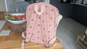 Pink corduroy nursery backpack with strawberry print sitting packed on a wooden dining table.
