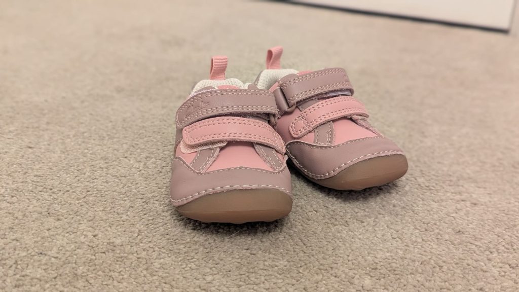 Pair of small pink and grey leather Clarks velcro shoes sitting on a carpet ready for a first day at nursery