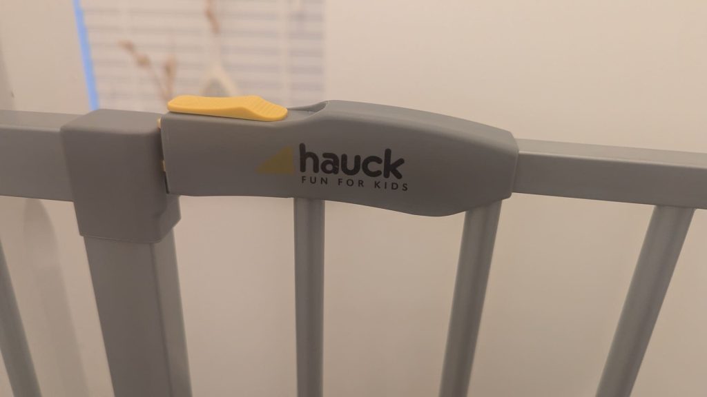 Close-up of the grey handle and yellow sliding lock catch on a Hauck safety gate.