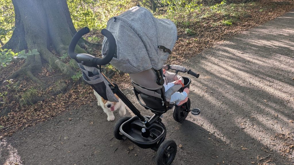 Rear perspective of a child in a grey Kinderkraft tricycle review model showing the sun hood and parent steering handle.