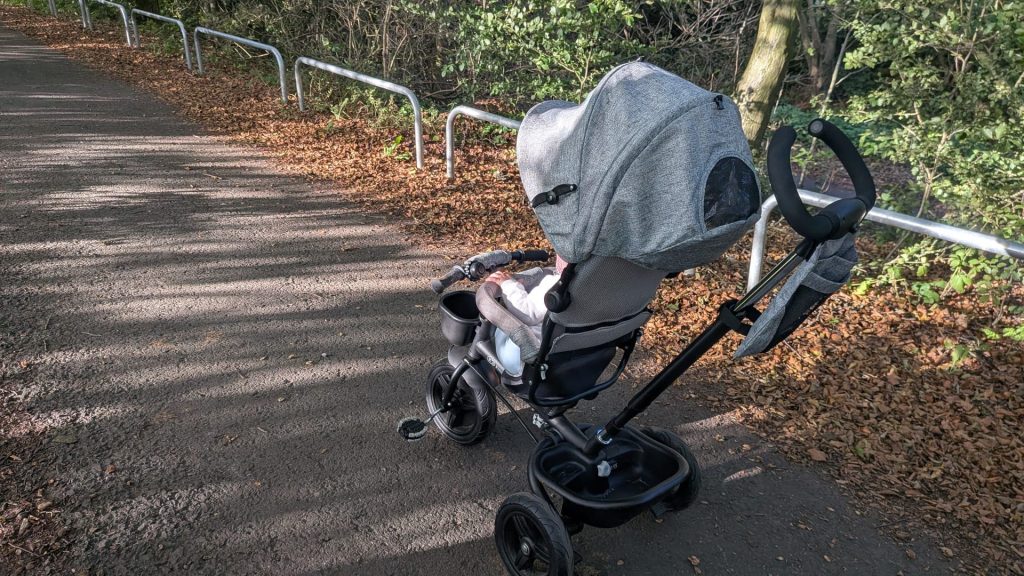 Side view of a grey Kinderkraft tricycle review unit parked on a shaded park path.